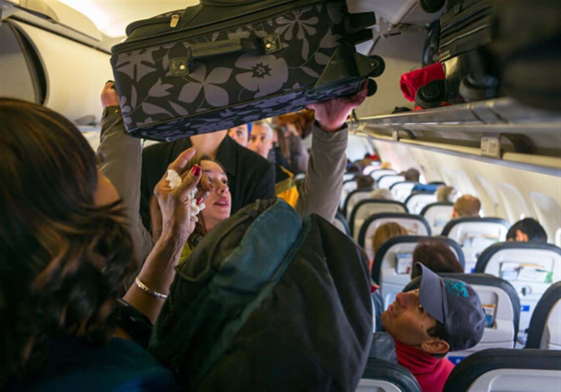 women putting luggage in overhead bin on a flight to colorado