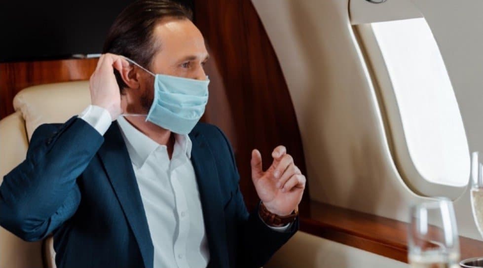 Man looking out of a plane window while putting on a mask. Private Aviation | LIVT | COVID19 | Covid Impact | Aviation Industry